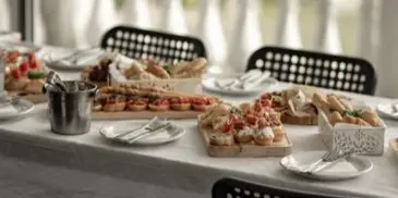 A long table set with a white tablecloth, displaying an assortment of appetizers, bread, and plated food ready for a catering event.