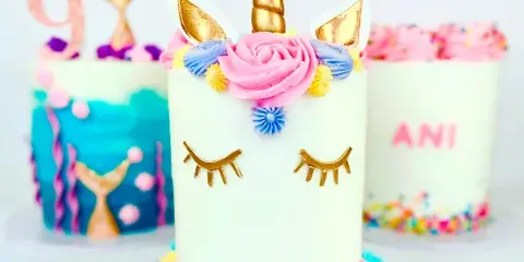 A white unicorn-themed cake with a gold horn, ears, and closed eyes, decorated with colorful frosting flowers.