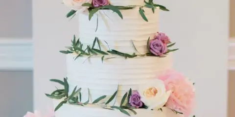 A four-tier white wedding cake decorated with pink and purple roses and greenery.