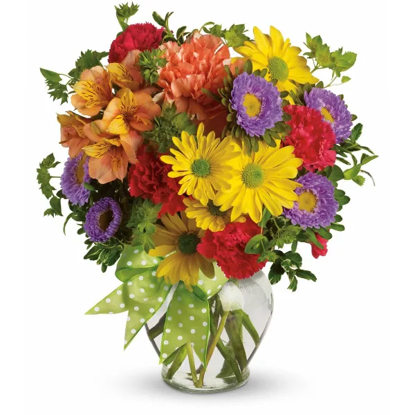 A colorful mixed bouquet of flowers including yellow daisies, red carnations, and purple chrysanthemums in a clear glass vase with a green polka-dot ribbon.
