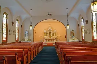 Interior view of a historic church with wooden pews, stained glass windows, and an altar.