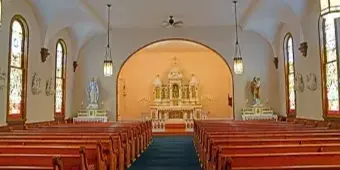 Interior view of a historic church with wooden pews, stained glass windows, and an altar.