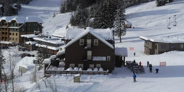 Snow-covered mountain lodge with outdoor dining tables and a sign reading 'Open Daily at 11:00 am'