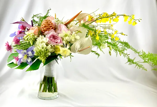 A colorful floral arrangement with pink roses, white orchids, and greenery in a clear glass vase.