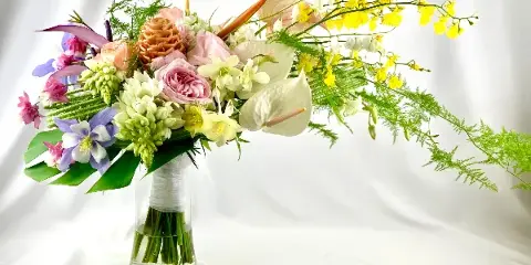 A colorful floral arrangement with pink roses, white orchids, and greenery in a clear glass vase.