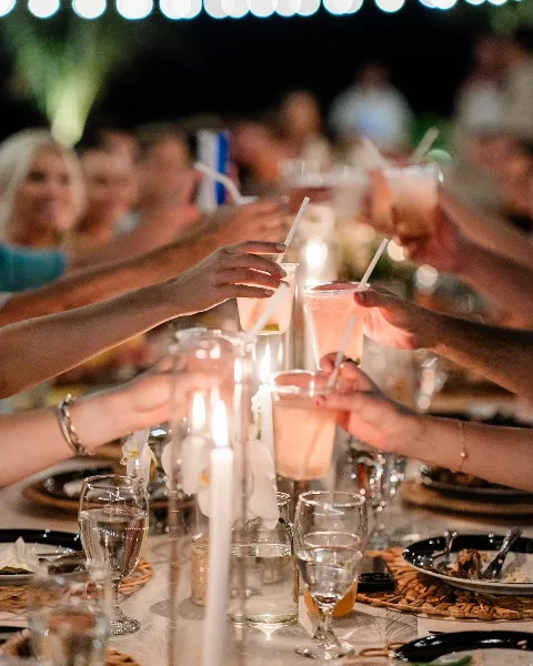 Guests toasting with drinks at a wedding reception table featuring floral centerpieces and candles.