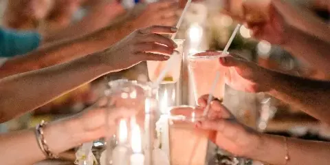 Guests toasting with drinks at a wedding reception table featuring floral centerpieces and candles.