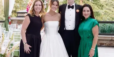 A bride and groom posing with two women in formal attire at a decorated wedding venue with floral arrangements and white drapery.