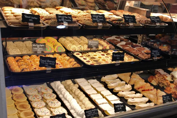 A bakery display case filled with an assortment of cookies, pastries, and cakes with handwritten price tags.