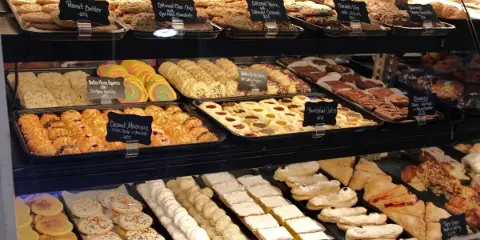 A bakery display case filled with an assortment of cookies, pastries, and cakes with handwritten price tags.