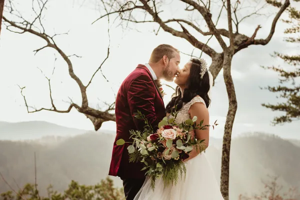 A bride and groom sharing a kiss outdoors with a mountainous landscape in the background.