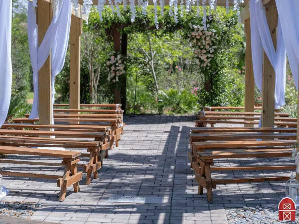Outdoor wedding ceremony setup with rows of wooden benches and a floral archway.