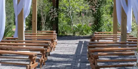 Outdoor wedding ceremony setup with rows of wooden benches and a floral archway.