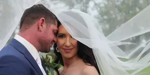 A bride and groom posing for a wedding portrait with the bride's veil blowing in the wind.