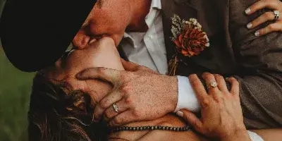 A bride and groom sharing a kiss, with the groom wearing a black cowboy hat and the bride in a white wedding dress.