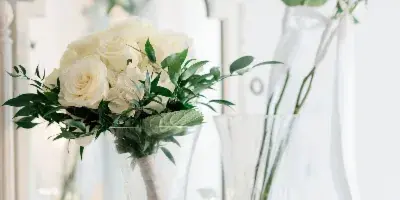 A vase of white roses and greenery sitting on a white dresser with a mirror in the background.