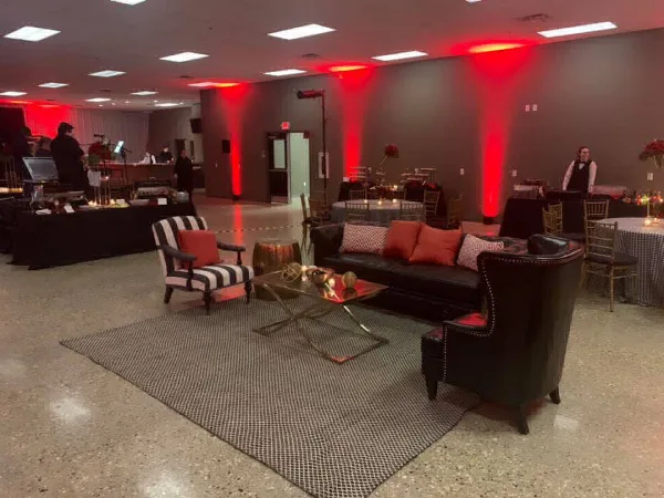 Interior view of a wedding reception venue with a lounge area, red accent lighting, and set dining tables.