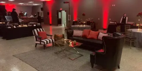 Interior view of a wedding reception venue with a lounge area, red accent lighting, and set dining tables.