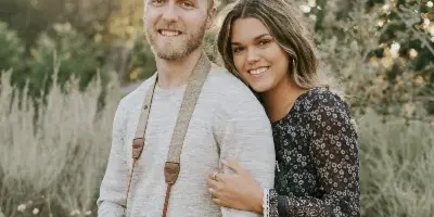 A smiling man and woman standing outdoors, both holding professional DSLR cameras.