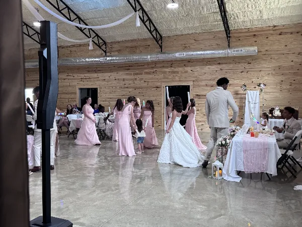 Interior view of The Landing event venue during a wedding reception, showing a bride, bridesmaids, and guests in a large room with wood walls and concrete floors.