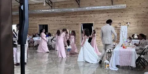Interior view of The Landing event venue during a wedding reception, showing a bride, bridesmaids, and guests in a large room with wood walls and concrete floors.