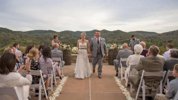 A bride and groom walking down the aisle during an outdoor wedding ceremony with guests seated on either side.