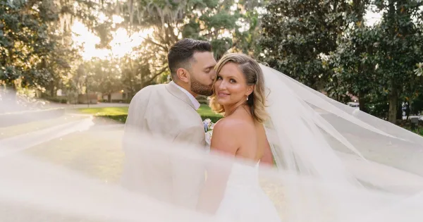 A bride and groom sharing a kiss outdoors with a soft-focus foreground and natural lighting.