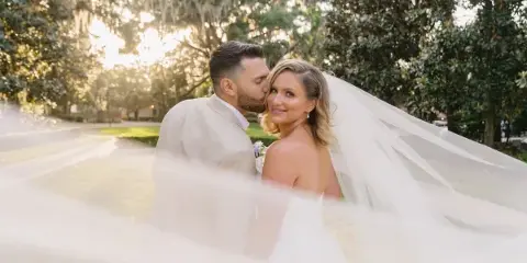 A bride and groom sharing a kiss outdoors with a soft-focus foreground and natural lighting.