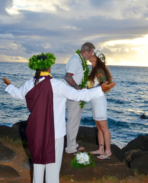 A wedding officiant in traditional attire officiating a beach wedding ceremony for a couple.