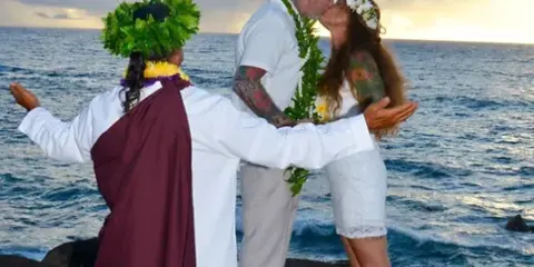 A wedding officiant in traditional attire officiating a beach wedding ceremony for a couple.