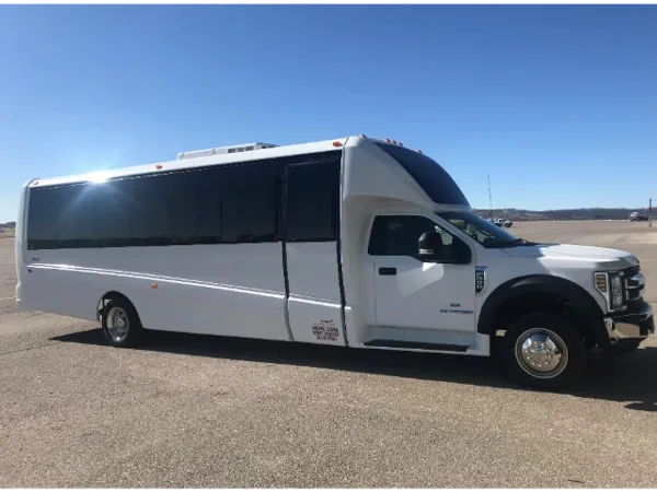 A white luxury executive mini-coach parked on a paved lot under a clear blue sky.