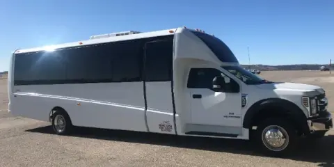 A white luxury executive mini-coach parked on a paved lot under a clear blue sky.