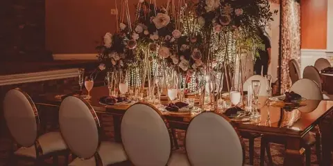 A luxury event table setting featuring upholstered chairs, glassware, and a large floral centerpiece in a geometric frame.