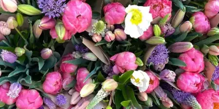 A close-up view of numerous fresh flower bouquets featuring pink peonies, tulips, and purple accents.