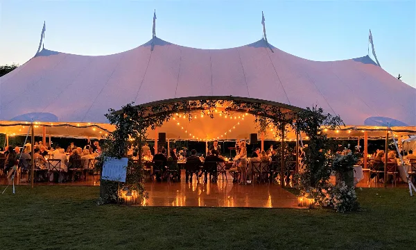A large white wedding tent at dusk with string lights, floral decorations, and a dance floor.