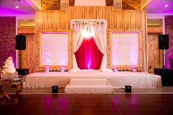 A decorated wedding stage featuring a dance floor, floral arch, and ornate gold frames.