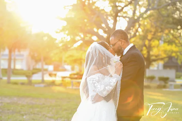 A wedding couple sharing a kiss outdoors in warm sunlight, with the Terry James Photography logo in the bottom right corner.