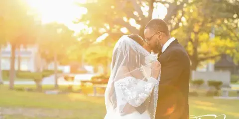 A wedding couple sharing a kiss outdoors in warm sunlight, with the Terry James Photography logo in the bottom right corner.