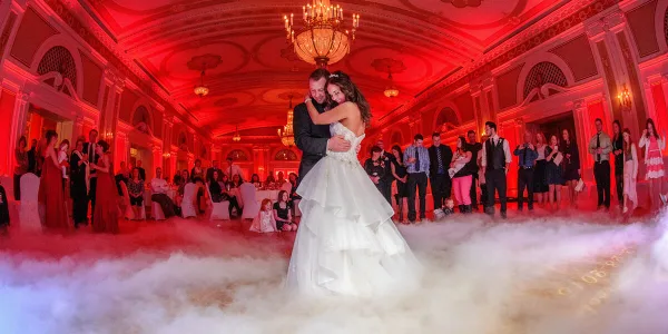 A bride and groom dancing at a wedding reception surrounded by low-lying fog effects and red up-lighting.