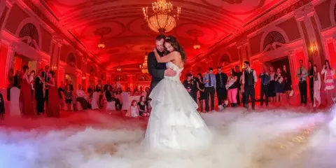 A bride and groom dancing at a wedding reception surrounded by low-lying fog effects and red up-lighting.