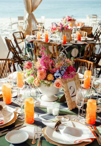 A professionally arranged outdoor event table featuring a vibrant floral centerpiece, table number, and fine dining place settings.