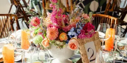A professionally arranged outdoor event table featuring a vibrant floral centerpiece, table number, and fine dining place settings.