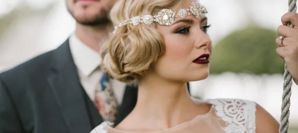 Close-up profile of a bride with vintage updo, jeweled headband, and professional makeup.