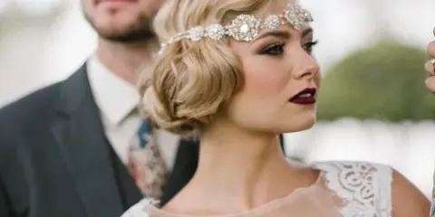 Close-up profile of a bride with vintage updo, jeweled headband, and professional makeup.