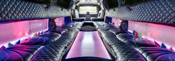 Interior view of a party bus with black leather seating and pink ambient lighting.