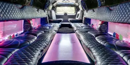 Interior view of a party bus with black leather seating and pink ambient lighting.