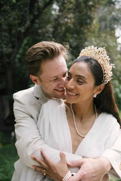 A bride and groom embracing and smiling outdoors in a natural setting.