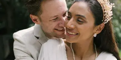 A bride and groom embracing and smiling outdoors in a natural setting.