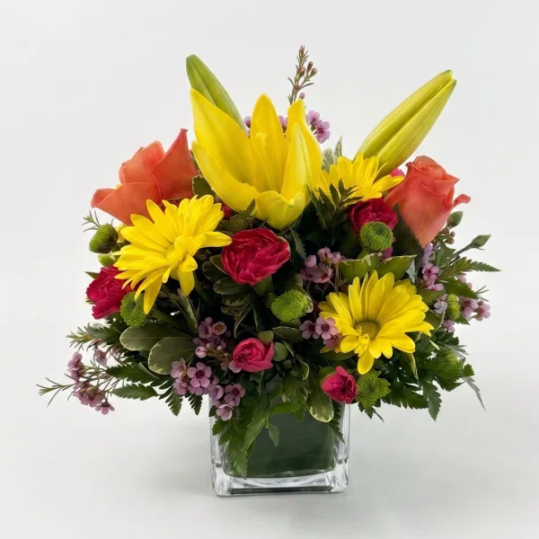 A vibrant floral arrangement featuring yellow lilies, orange roses, and yellow daisies in a clear glass vase.
