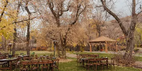 Outdoor event setup with wooden tables, chairs, and string lights in a park setting.